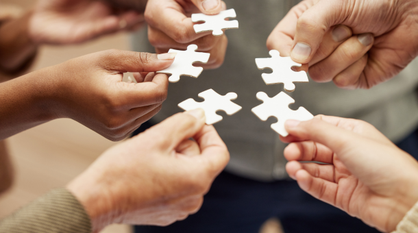 Five hands holding jigsaw puzzle pieces